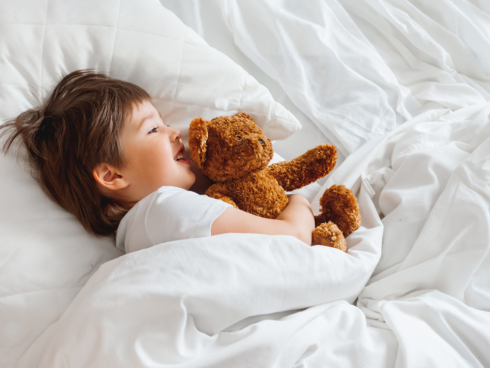 Kind liegt mit seinem Kuscheltier im Bett